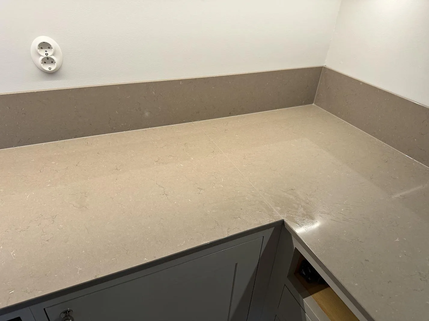 Polerad Silestone Coral Clay som L-formad köksbänkskiva med uppvikt stänkskydd i ett kök i Malmö.
