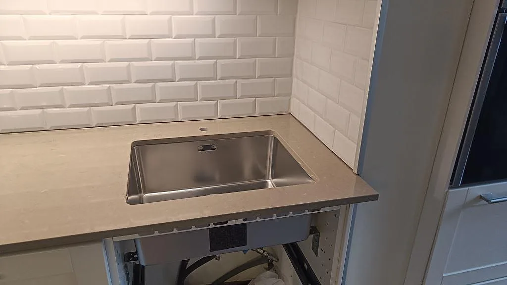 Underlimmad rostfri diskho i polerad köksbänkskiva av Silestone Coral Clay, gråbeige kvartskomposit, med vitt kakel i Malmö.