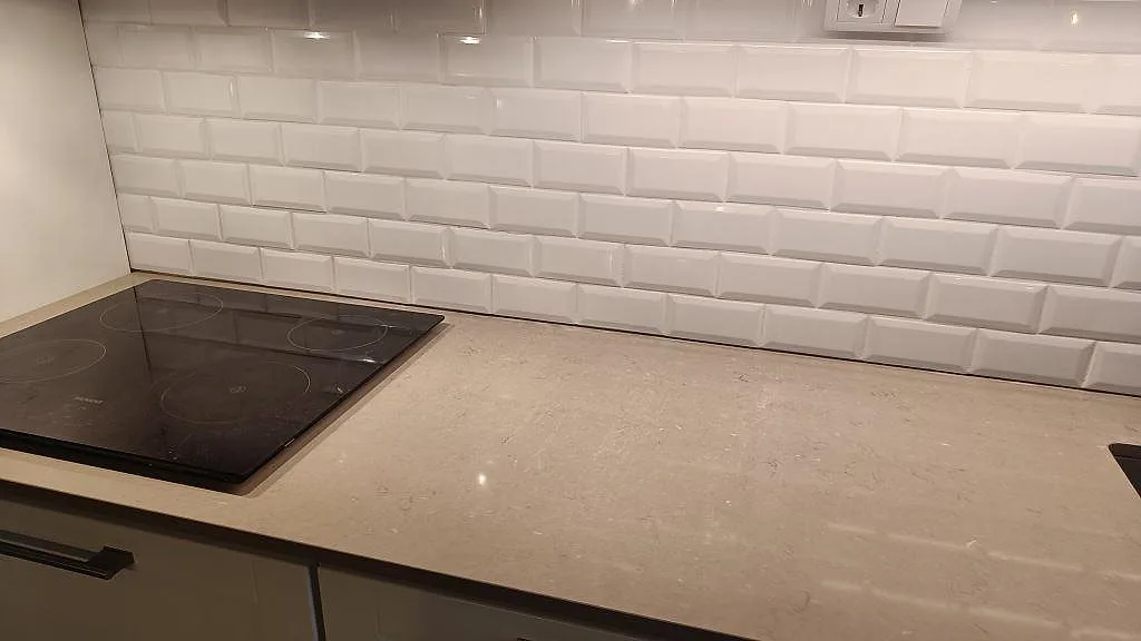 Närbild av polerad köksbänkskiva i Silestone Coral Clay, gråbeige kvartskomposit, vid häll och vitt kakel i Malmö.
