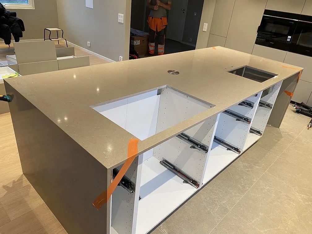 Vinklad vy över köksö i polerad Silestone Coral Clay med hällurtag, diskho och stenklädd gavel i ett kök i Malmö.