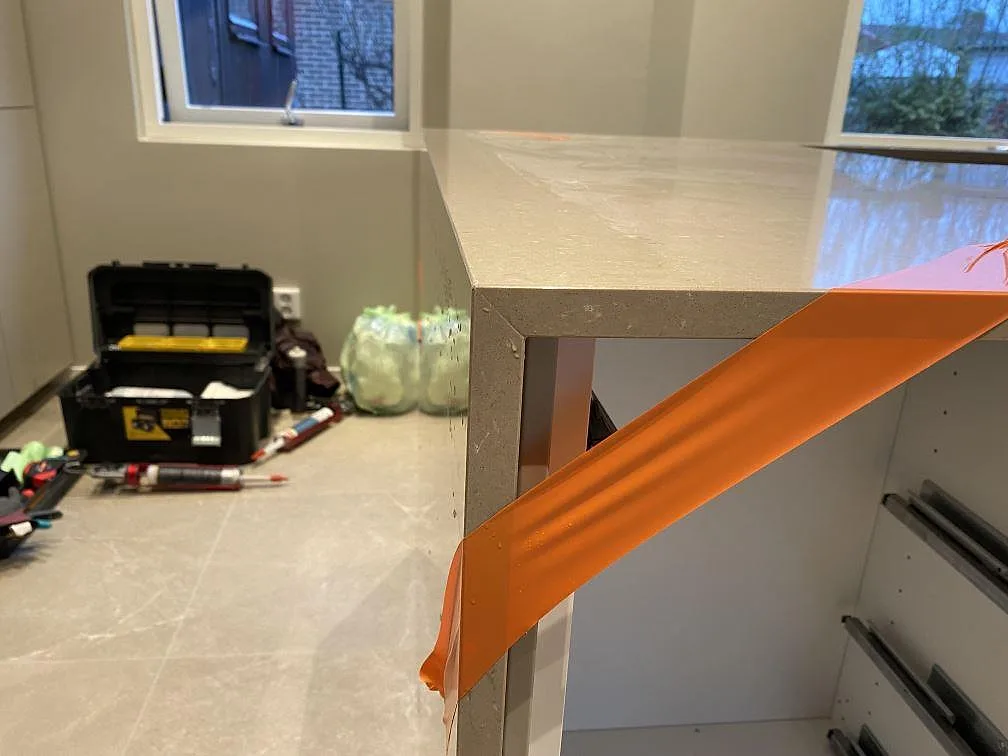 Närbild på framkant och stenklädd sida i polerad Silestone Coral Clay med monteringstejp på köksön i Malmö.