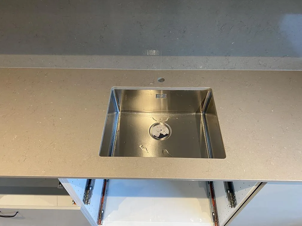 Närbild av rostfri diskho i polerad Silestone Coral Clay köksbänkskiva med blandarhål och stänkvägg i Malmö.