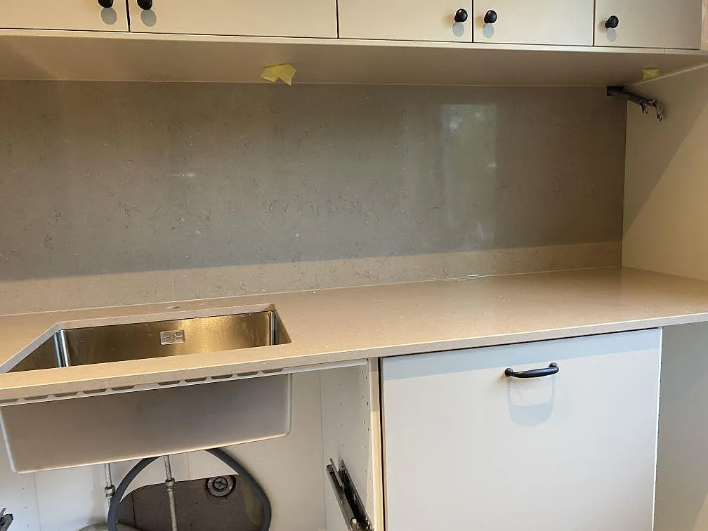 Polerad Silestone Coral Clay som köksbänkskiva och stänkvägg med rostfri diskho i ett ljust kök under montering i Malmö.