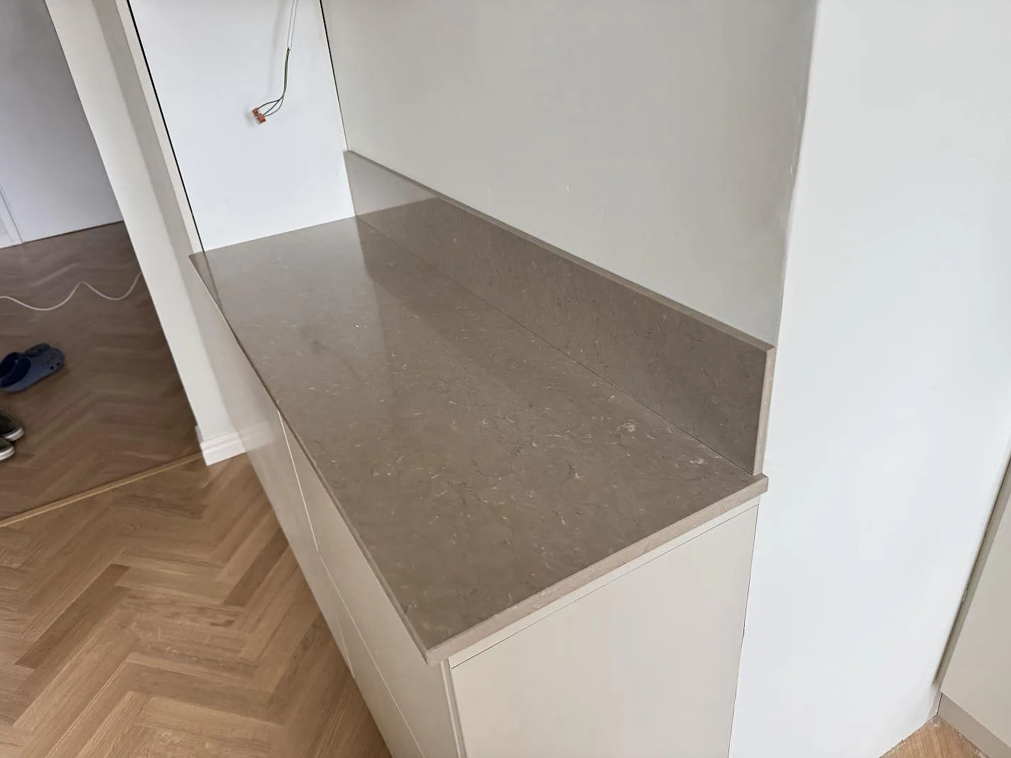 Sidobänk i polerad Silestone Coral Clay på vita köksstommar under montering i Malmö.