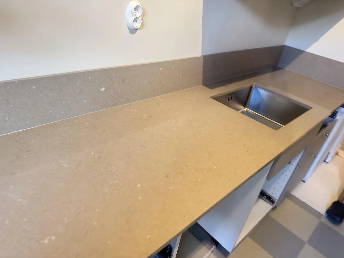 Lång arbetsyta i polerad Silestone Coral Clay med matchande stänkskydd och rostfri diskho under montering i Malmö.