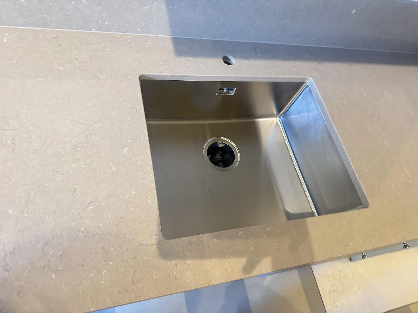 Närbild på underlimmad rostfri diskho och borrat blandarhål i polerad Silestone Coral Clay bänkskiva i Malmö.