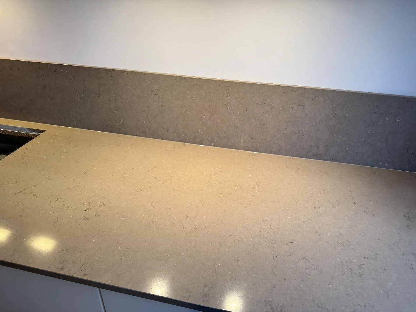 Bänkskiva i polerad Silestone Coral Clay med stänkskydd i greige komposit längs väggen i ett kök i Malmö.