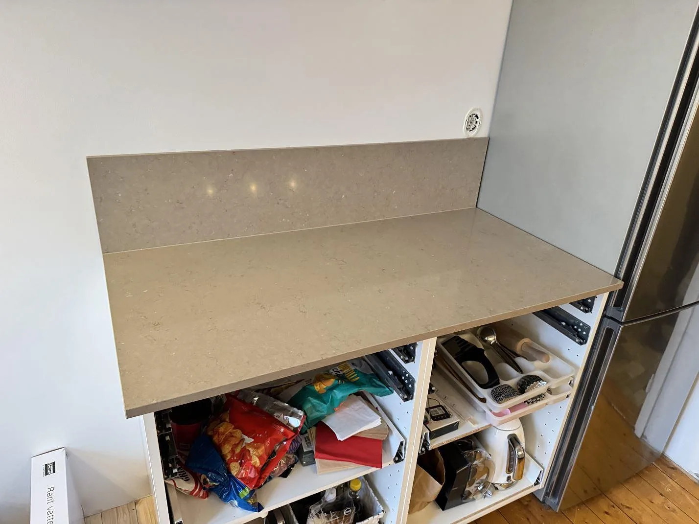 Köksbänkskiva i varm greige Silestone Coral Clay mot kylskåp med uppvikt stänkkant i ett kök i Malmö.