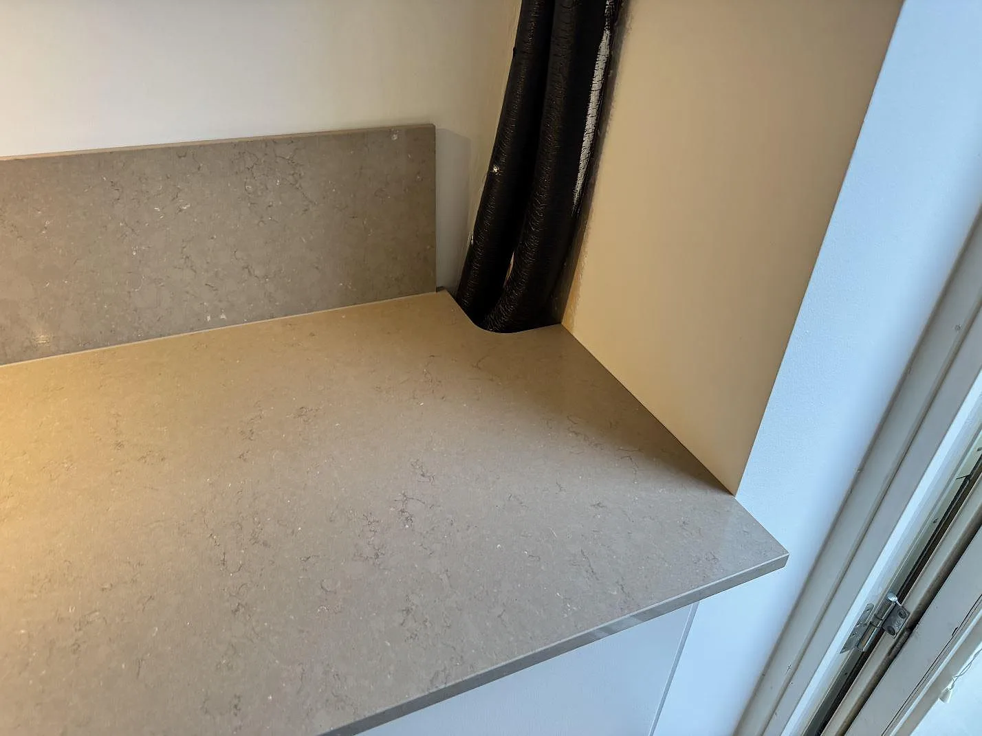 Hörn av köksbänk i Silestone Coral Clay med uppvikt stänkkant och synlig ventilationskanal under montering i Malmö.