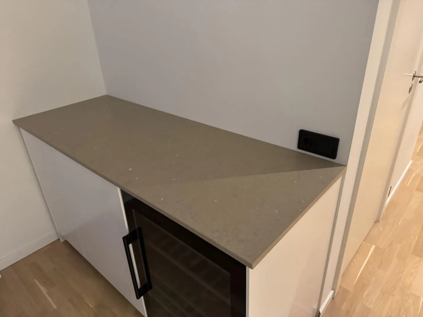 Beige Silestone Coral Clay köksbänkskiva i matt Mocka längs vita underskåp med vinkyl och eluttag, kök under montering i Malmö.