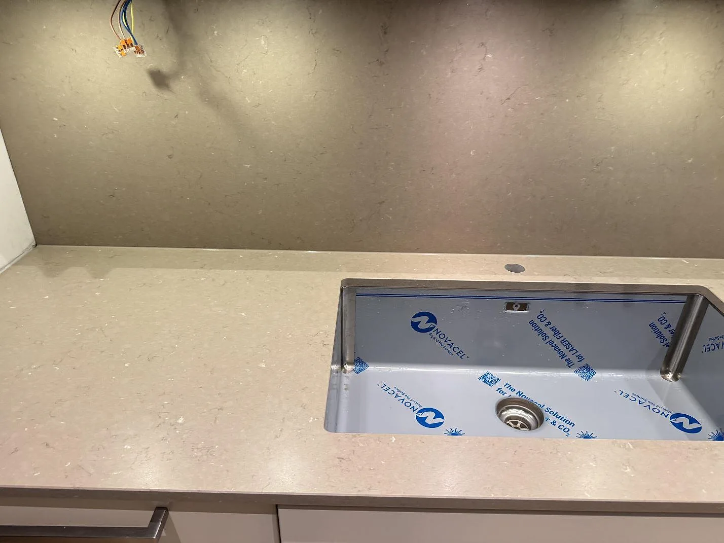 Närbild på underlimmad rostfri diskho i beige Silestone Coral Clay köksbänkskiva med borrat blandarhål och stänkskydd i samma sten, Malmö.