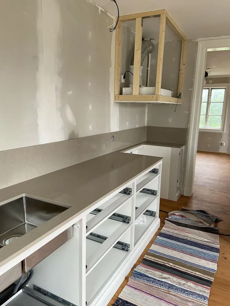 Köksbänkskiva i greige Silestone Coral Clay, polerad, monterad längs en köksdel med underlimmad rostfri diskho i ett kök under montering i Mölltorp.