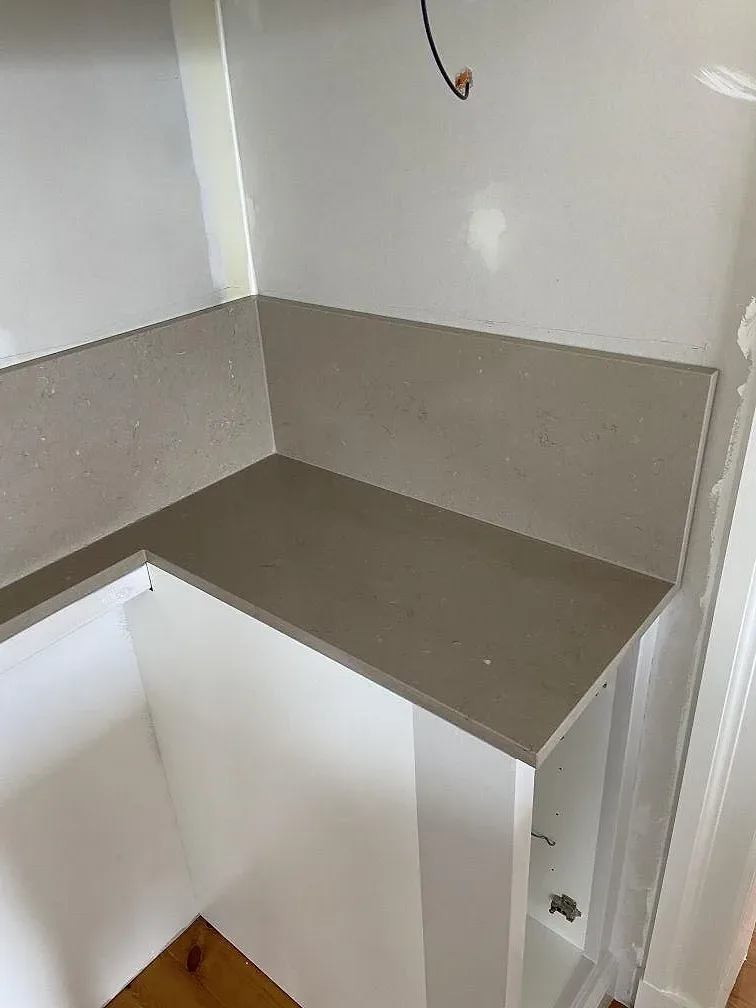 Greige Silestone Coral Clay bänkskiva med låg uppvikt stänkkant i sten runt ett hörn i ett kök under montering i Mölltorp.