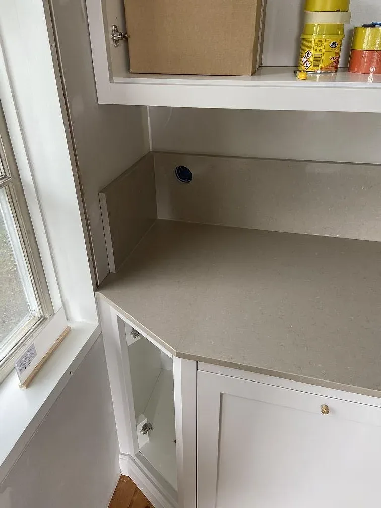 Detalj av polerad greige Silestone Coral Clay bänkskiva med stenstänkkant i ett kök under montering i Mölltorp.