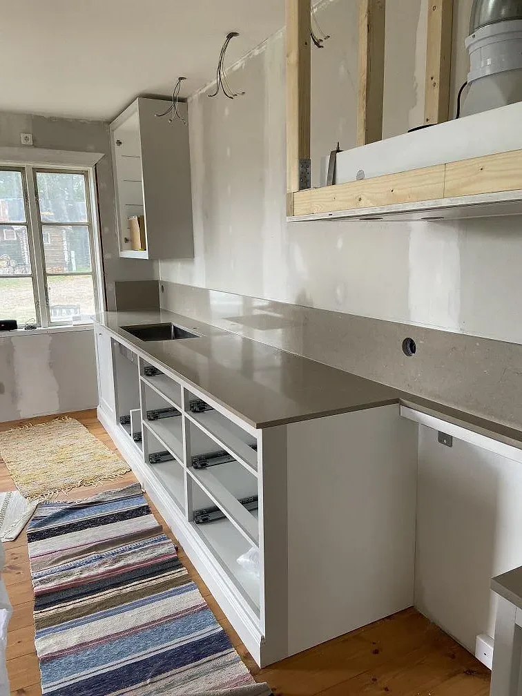 Polerad Silestone Coral Clay bänkskiva på vita stommar med köksö och rag i ett kök mitt under installation i Mölltorp.