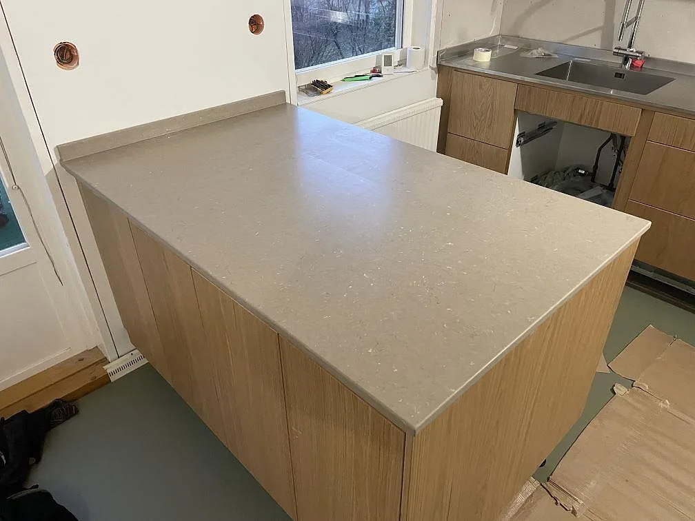 Köksö och väggbänk i matt Silestone Coral Clay, 20 mm kvartskomposit, med varm greige yta under montering i Mölnlycke.