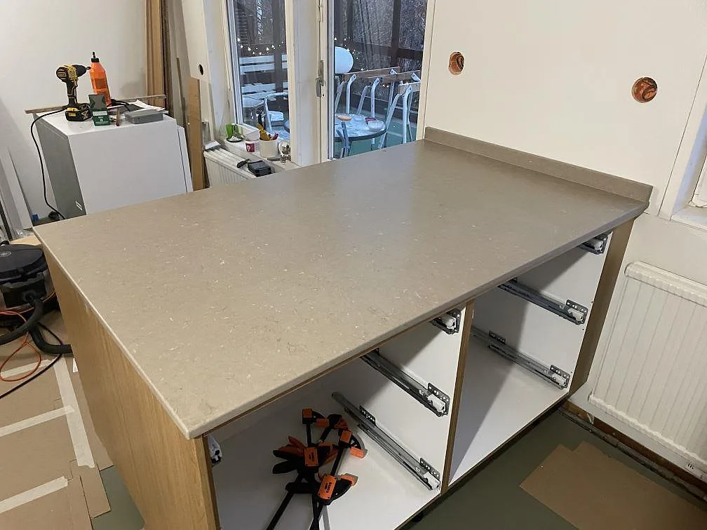 Köksbänk i matt Silestone Coral Clay, 20 mm kvartskomposit, med uppvikt stänkkant och öppna köksstommar i Mölnlycke.