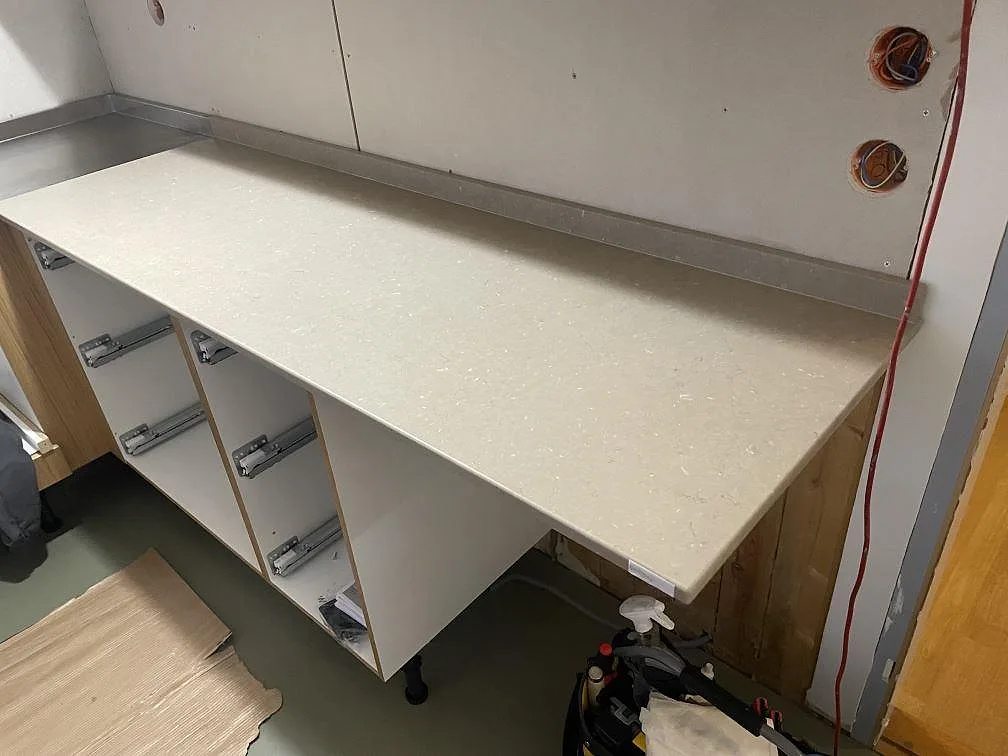 Rak väggbänk i matt Silestone Coral Clay med låg uppvikt stänkkant och öppna köksstommar under montering i Mölnlycke.