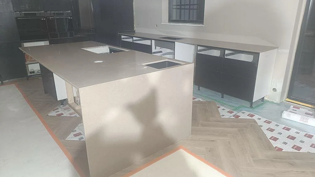 Köksbänkskiva och stort köksö i varm greige Silestone Coral Clay, polerad komposit, under montering i ett kök i Mörrum.