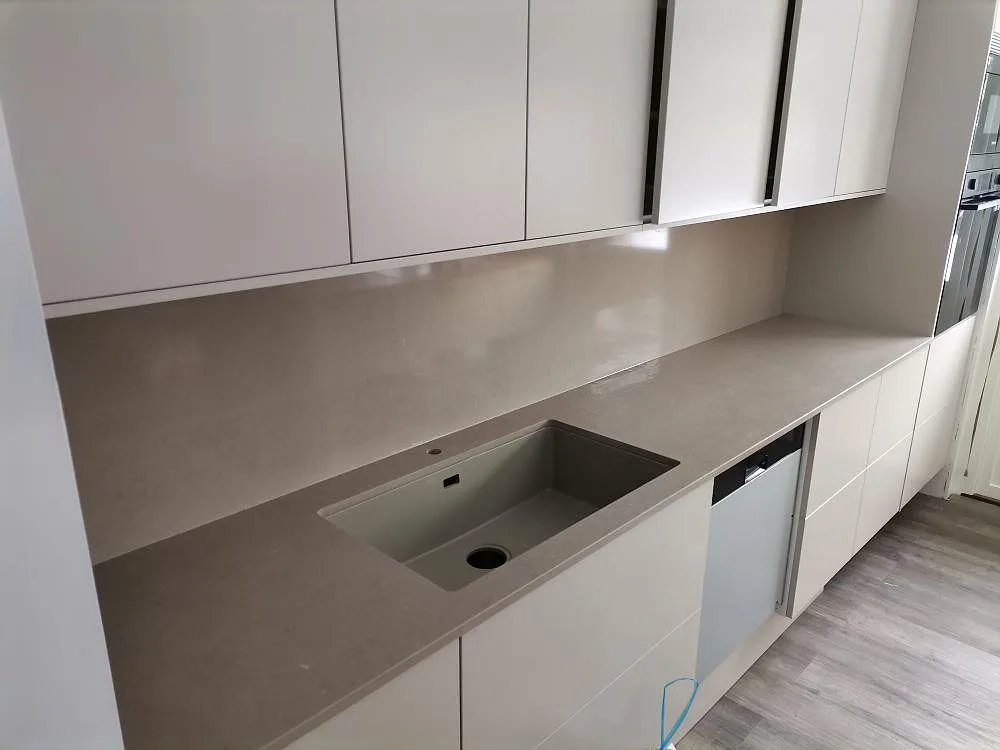 Köksbänkskiva i Silestone Coral Clay, polerad varm greige kvartskomposit, med underlimmad komposithoar och uppvikt stänkskydd i samma sten i ett kök i Motala.