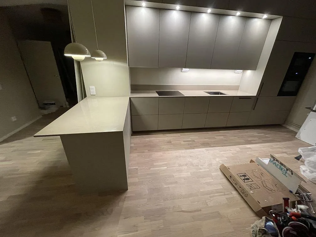 Köksbänkskiva i Silestone Coral Clay, polerad beige kvartskomposit, med halvö och lång väggsektion med induktionshäll och diskho i ett kök i Nacka.