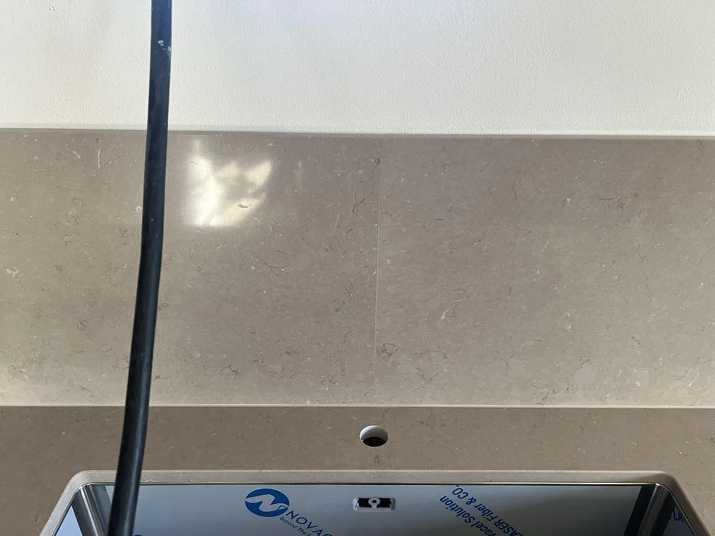 Detalj av stänkskydd och blandarhål vid svart underlimmad diskho i Silestone Coral Clay i Nättraby.