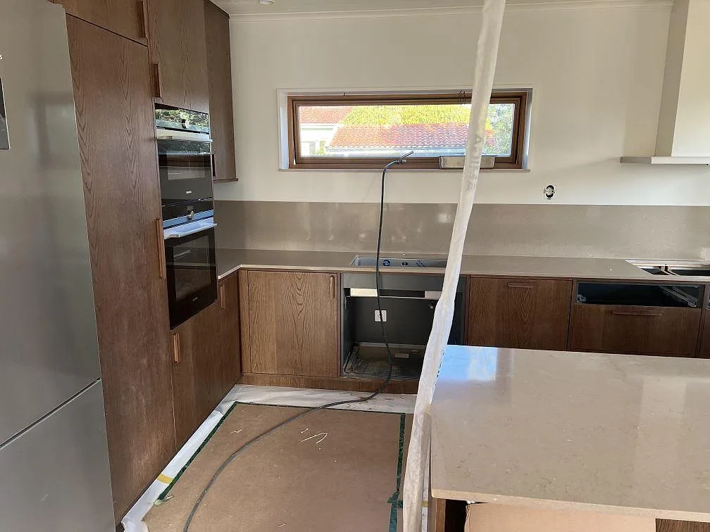 Polerad köksbänkskiva i Silestone Coral Clay med stänkskydd, köksö och valnötsbrun köksinredning i Nättraby.