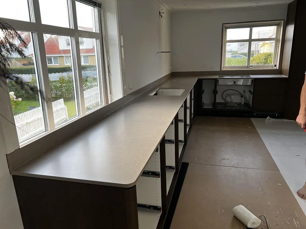 Lång köksbänkskiva i matt Silestone Coral Clay med uppvikt stänkkant längs stora fönster i ett kök i Öckerö.