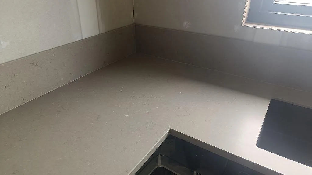 Hörnvy av Silestone Coral Clay bänkskiva med uppvikt stänkskydd och urtag i ett kök i Öckerö.