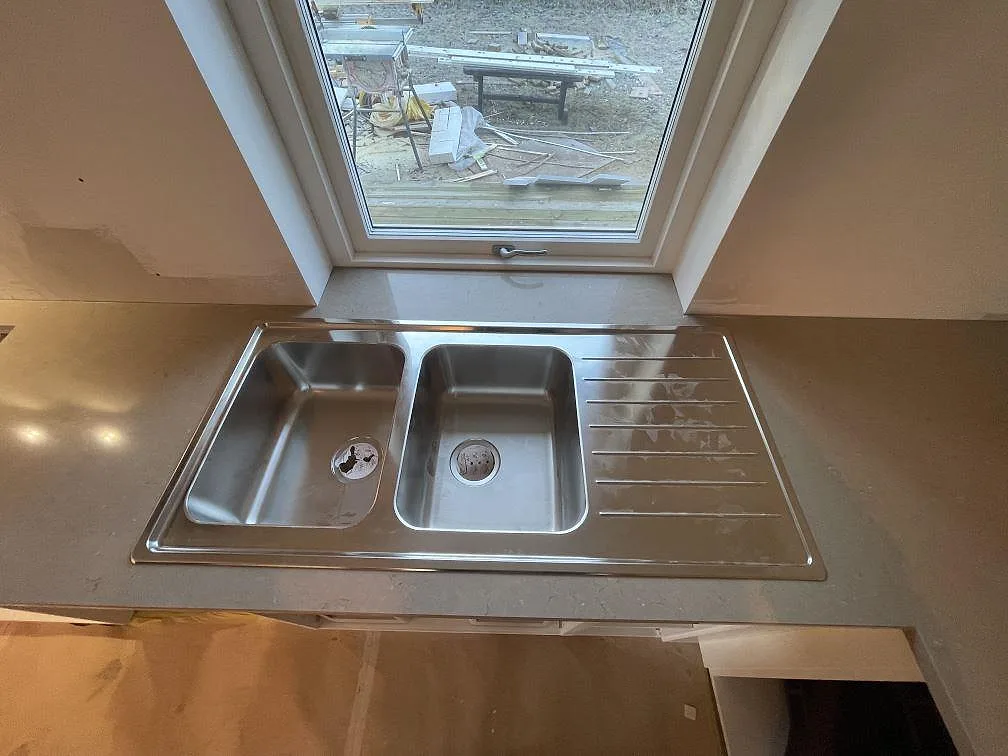 Ovanpåmonterad dubbelho i rostfritt stål i en polerad Silestone Coral Clay köksbänkskiva i Ösmo.