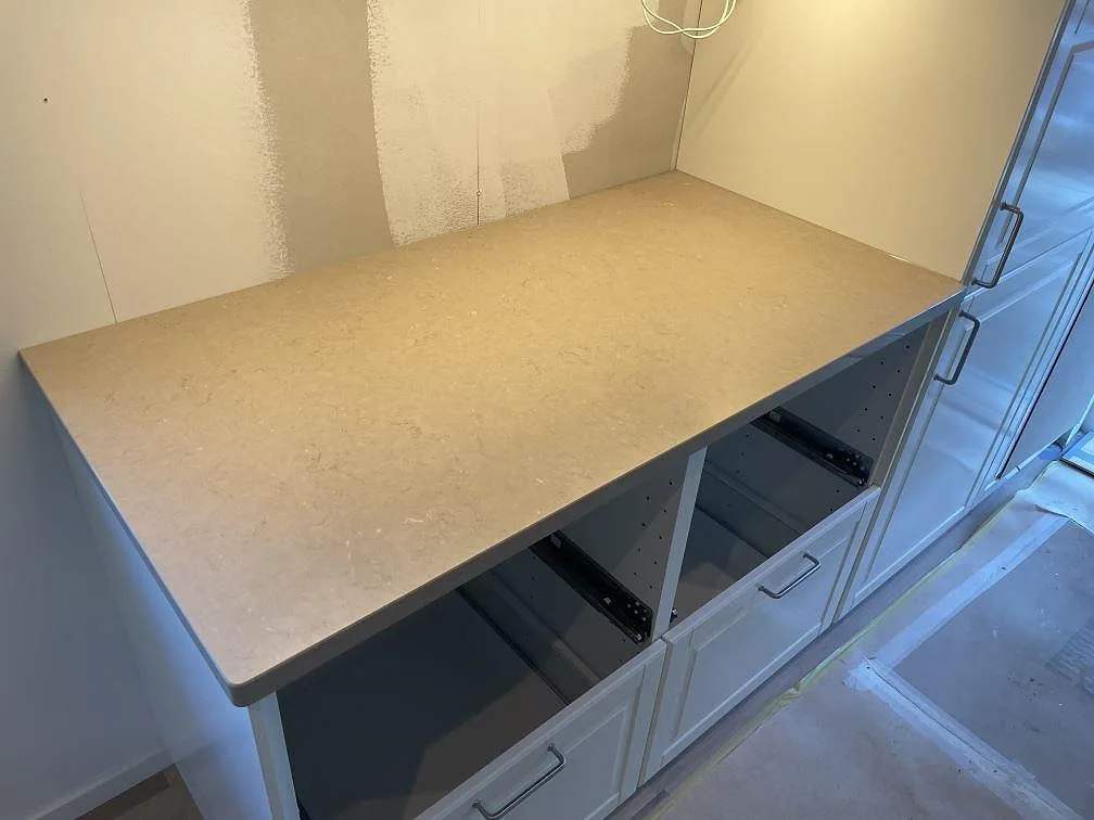 Rak bänkskiva i 30 mm polerad Silestone Coral Clay på vita köksstommar under montering i Ösmo.