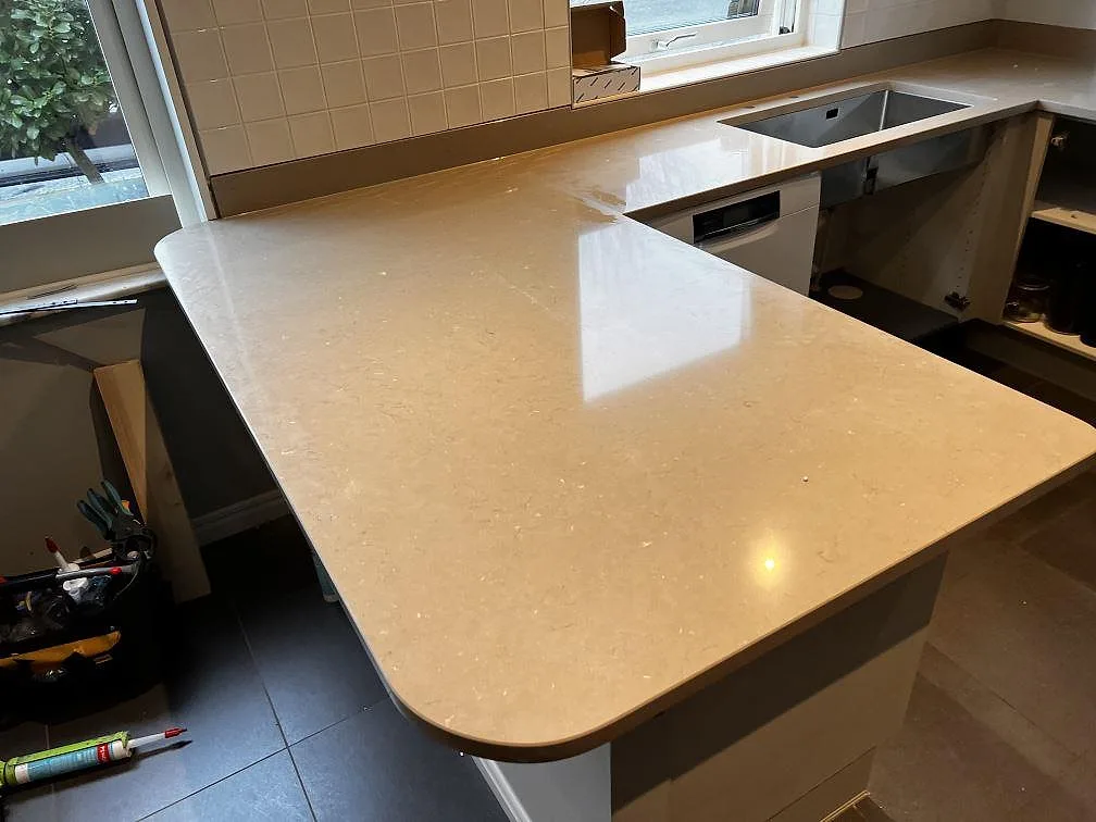 Polerad köksbänkskiva i Silestone Coral Clay med rundad halvö och rostfri diskho vid fönster i Oxie.