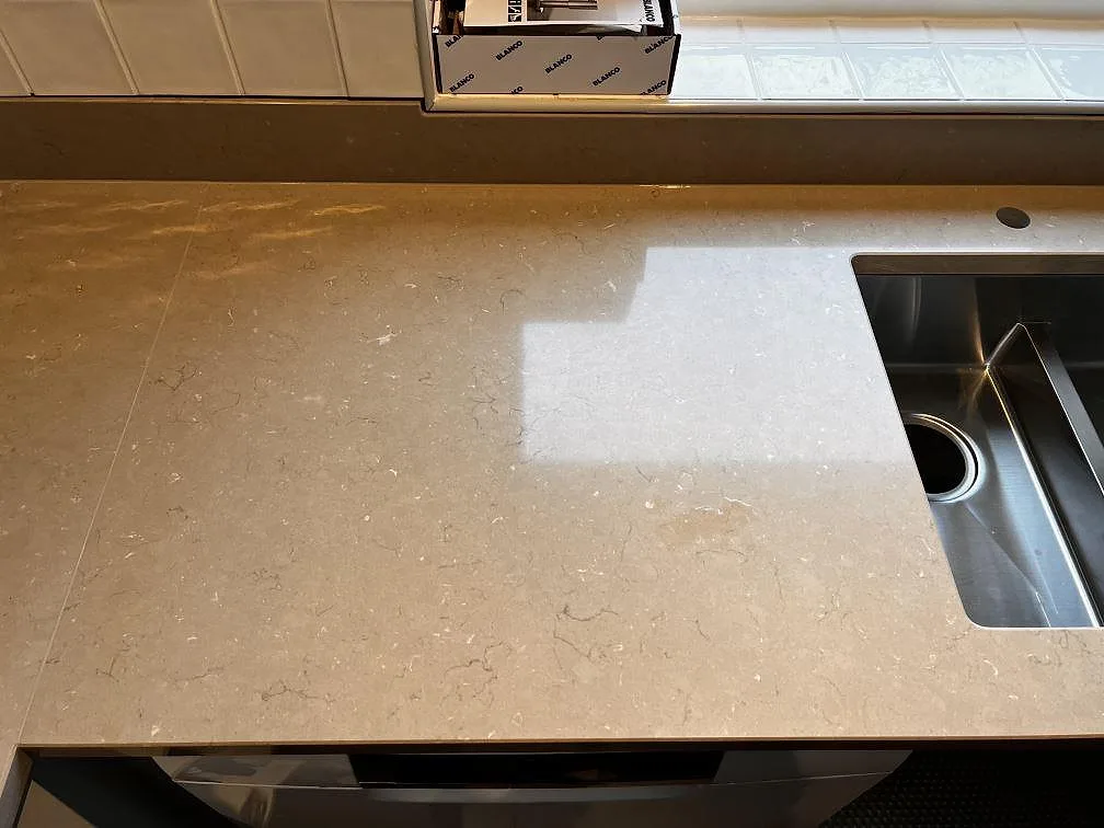 Bänkyta i polerad Silestone Coral Clay med rostfri diskho, blandarhål och fönsterljus i ett kök i Oxie.