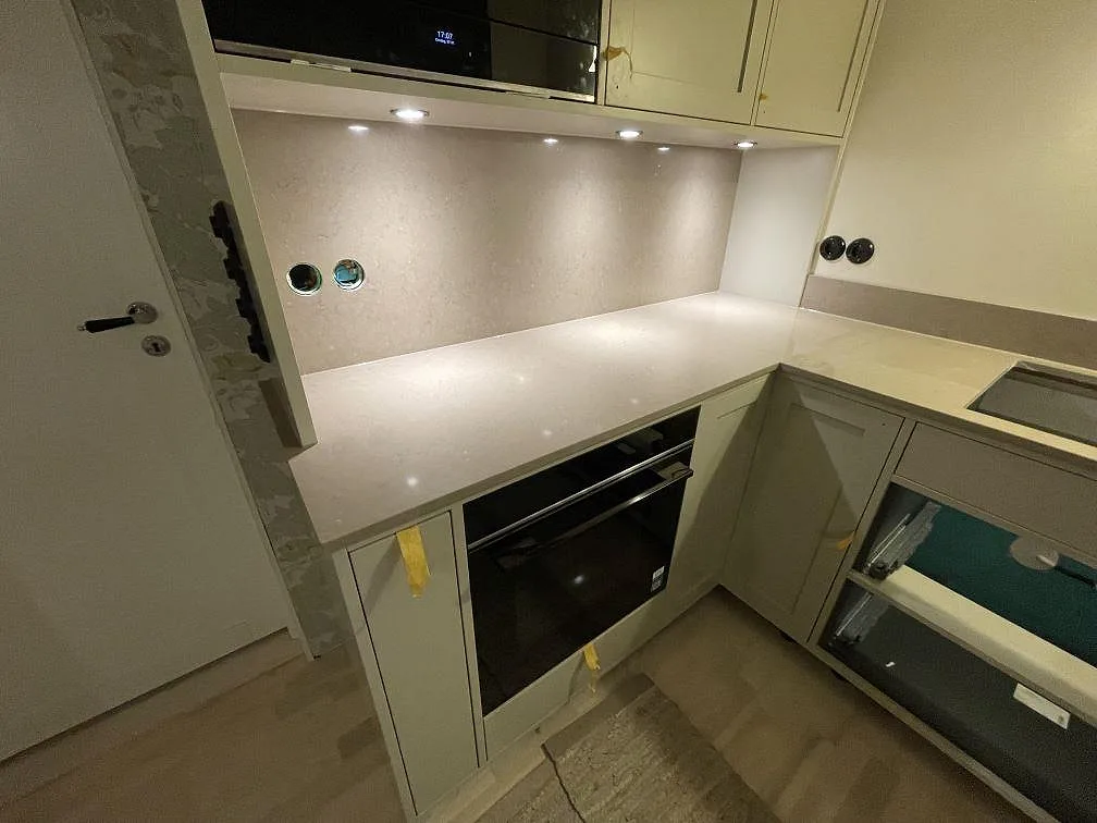 Polerat 12mm stänkskydd i Silestone Coral Clay som uppvikt kant med infällda eluttag, ovanför inbyggd ugn på en kort köksvägg i Saltsjö-Boo.