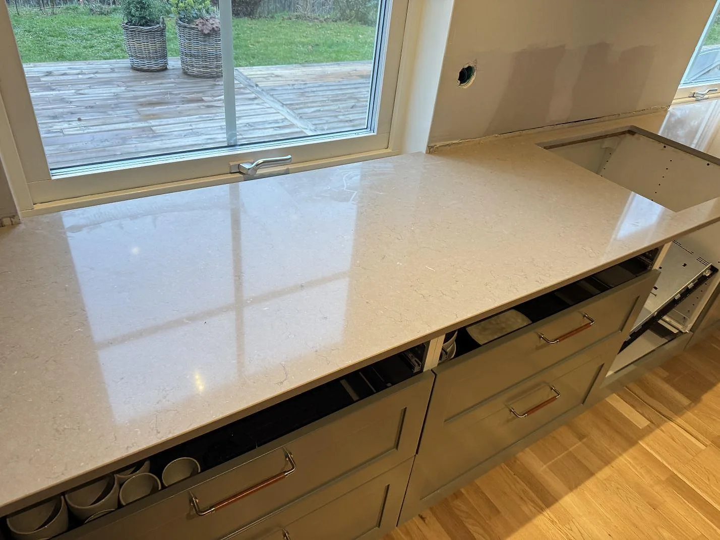 Silestone Coral Clay bänkskiva i polerad komposit framför fönster, med hälluttag och öppen köksstomme i Saxtorp.