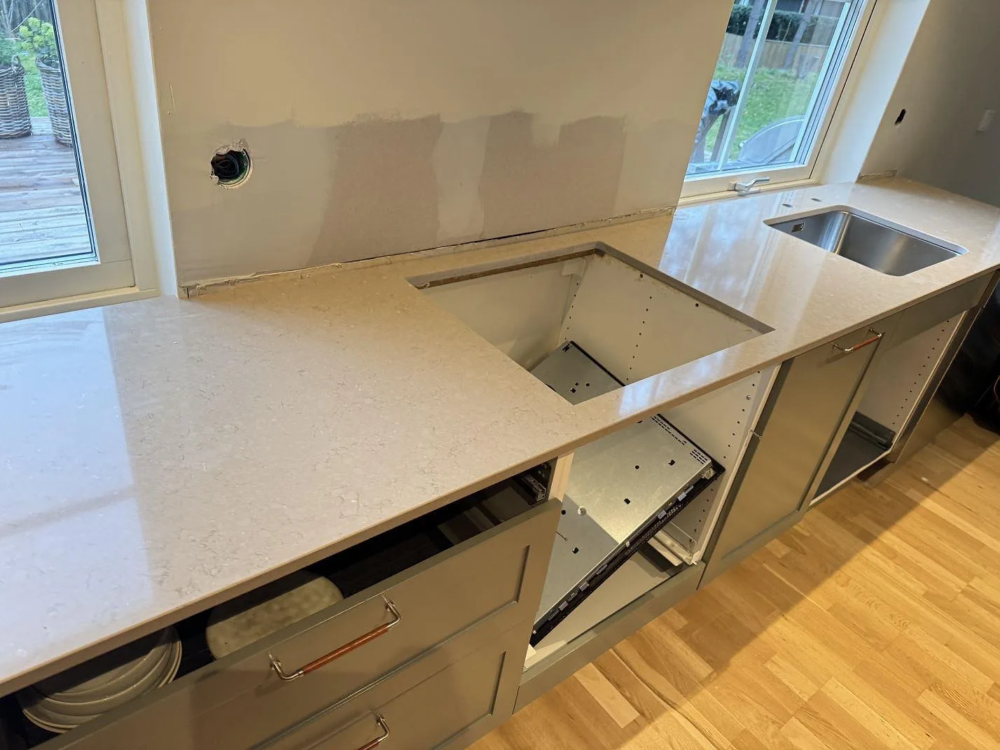Polerad köksbänkskiva i Silestone Coral Clay med rostfri diskho och förberett hälluttag under montering i Saxtorp.