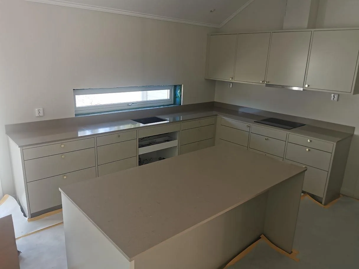 Köksbänkskiva och köksö i varm gråbeige Silestone Coral Clay, polerad komposit, med låg stänkkant och infälld häll i ett kök i Sigtuna.