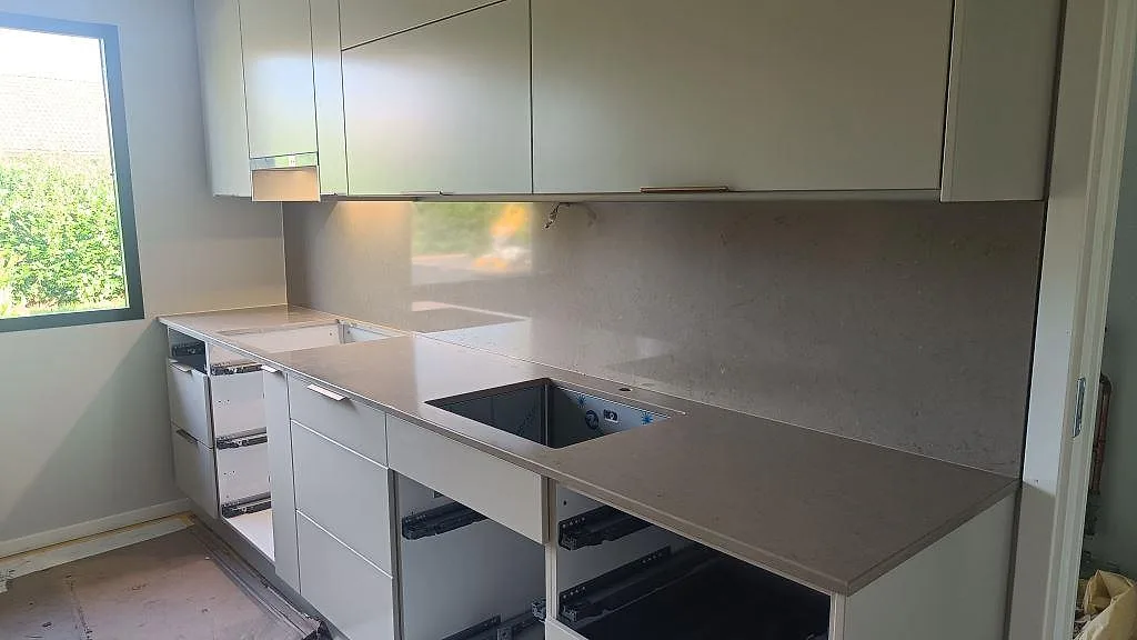 Rak köksbänkskiva i polerad Silestone Coral Clay komposit med underlimmad diskho, hällöppning och stänkvägg i ett ljust kök i Simrishamn.