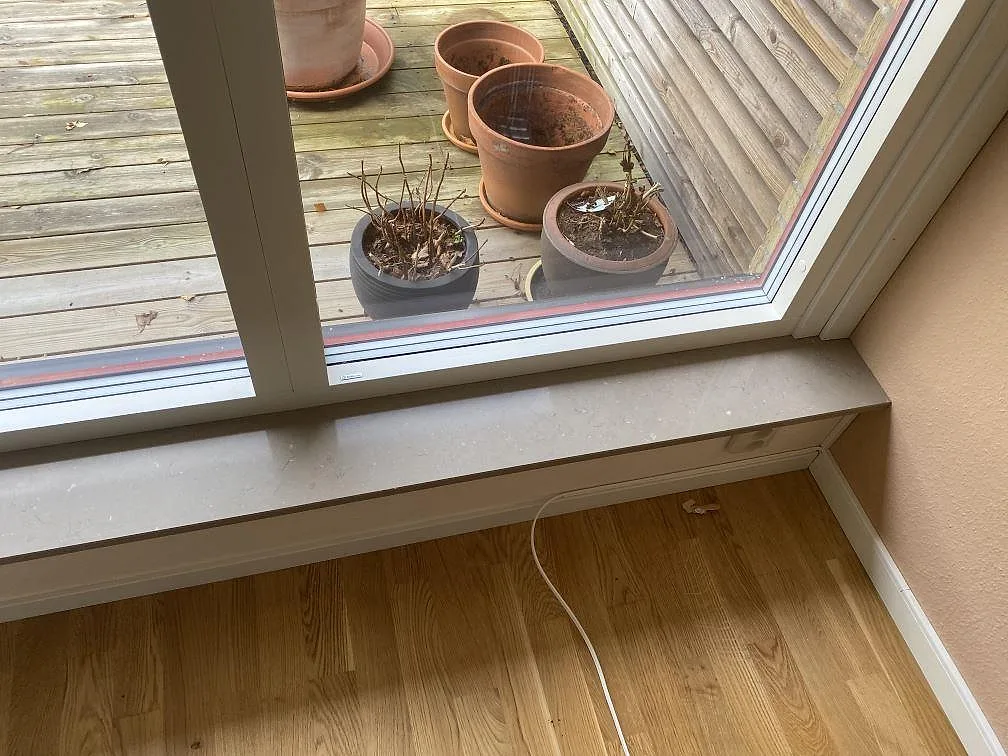 Fönsterbänk i Silestone Coral Clay i samma polerade greige sten som köksbänkskivan, med utsikt mot altanen i Skanör.