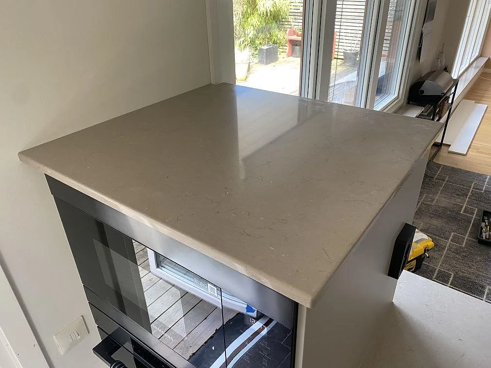 Polerad köksbänkskiva i Silestone Coral Clay över inbyggd ugn, med dagsljus från fönsterpartiet, i ett kök i Skanör.