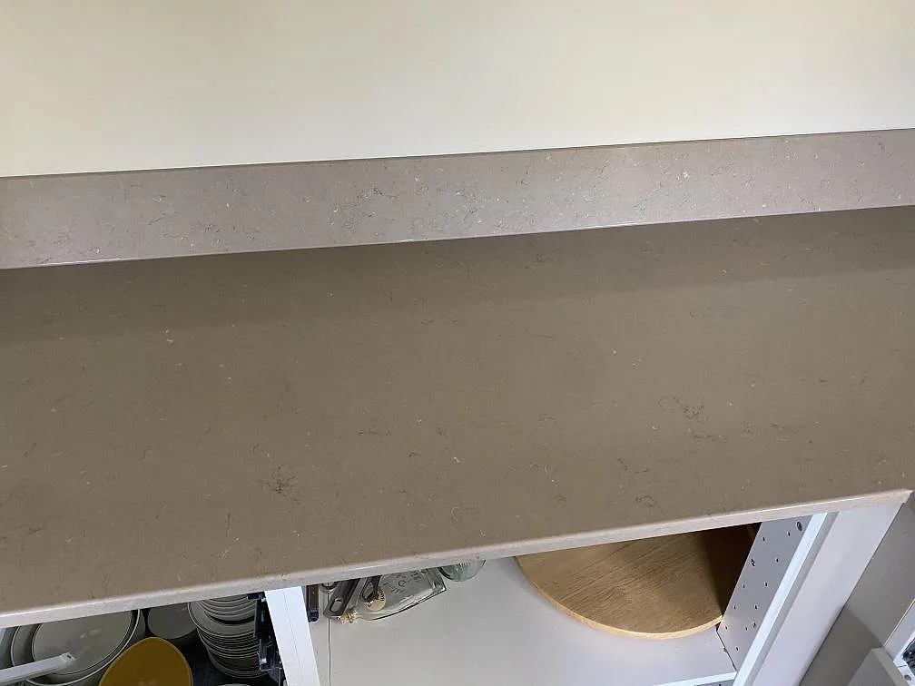 Polerad Silestone Coral Clay bänkskiva med uppvikt stänkkant längs väggen i ett kök under montering i Skanör.