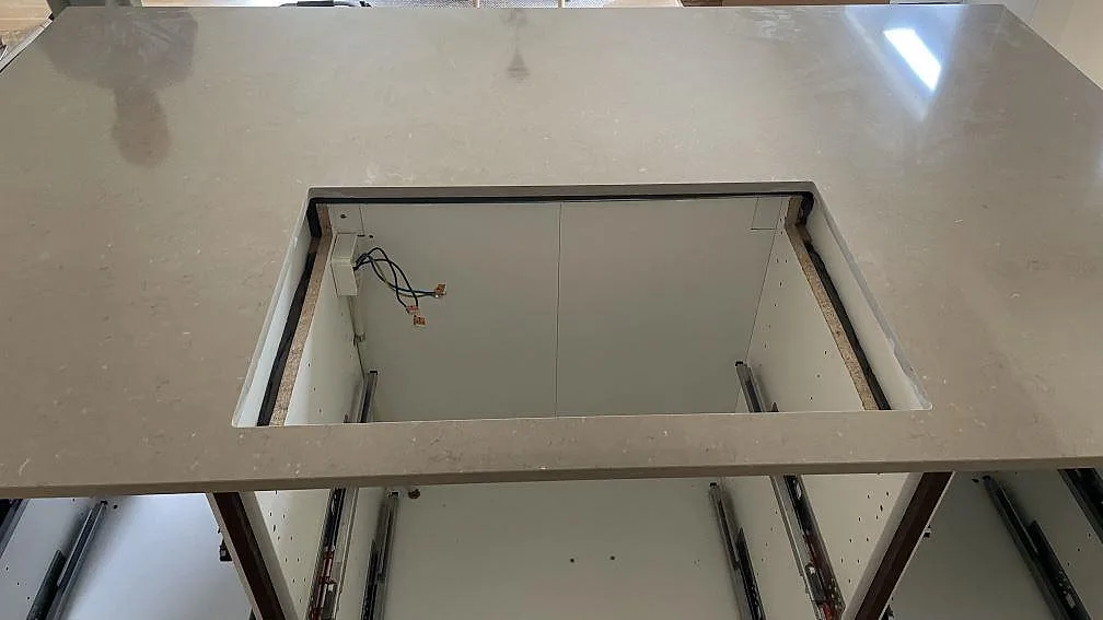 Detalj av hällöppning i polerad Silestone Coral Clay, 20 mm, på en köksö under montering i Skanör.