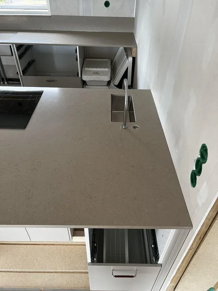 Närbild på polerad Silestone Coral Clay som bänkskiva med köksblandare, svart induktionshäll och stänkskydd i Skövde.
