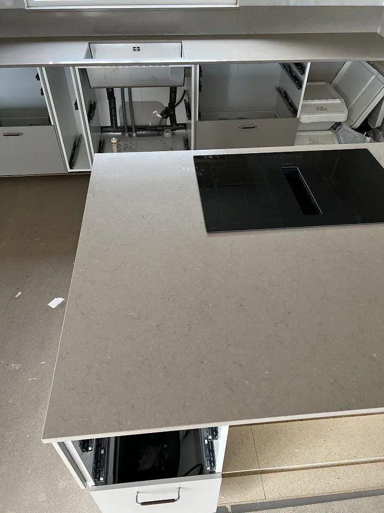 Detalj av polerad Silestone Coral Clay som köksbänkskiva med svart häll och öppna skåpstommar under montering i Skövde.