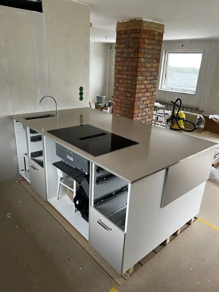 Polerad köksbänkskiva i Silestone Coral Clay runt en svart induktionshäll i ett U-format kök under montering i Skövde.