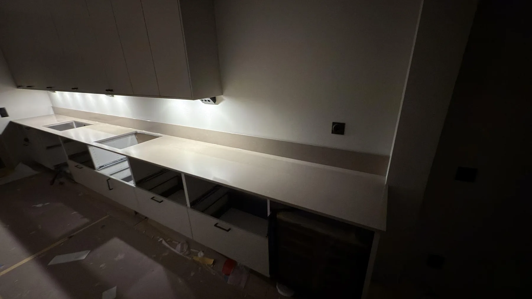 Köksbänkskiva i Silestone Coral Clay under en vinklad spiskåpa med undercabinet-belysning i ett kök i Skogås, taget under montering.