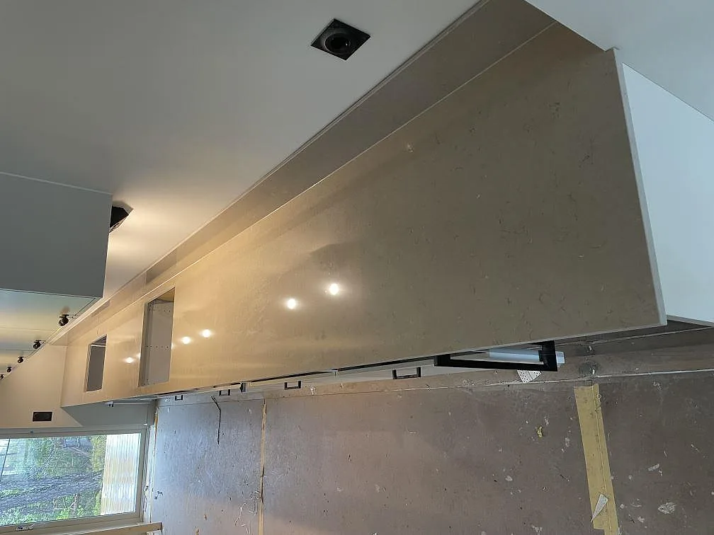 Polerad köksbänkskiva i Silestone Coral Clay monterad mot väggskåpen med reflektioner från köksbelysningen, under montering i ett kök i Skogås.