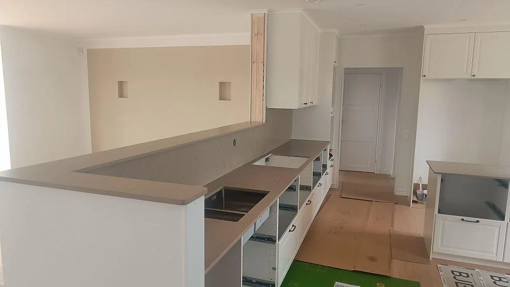 Köksbänkskiva i Silestone Coral Clay, matt Mocka-finish, med halvö, rostfri dubbelho och hällöppning i ett vitt kök i Skurup.