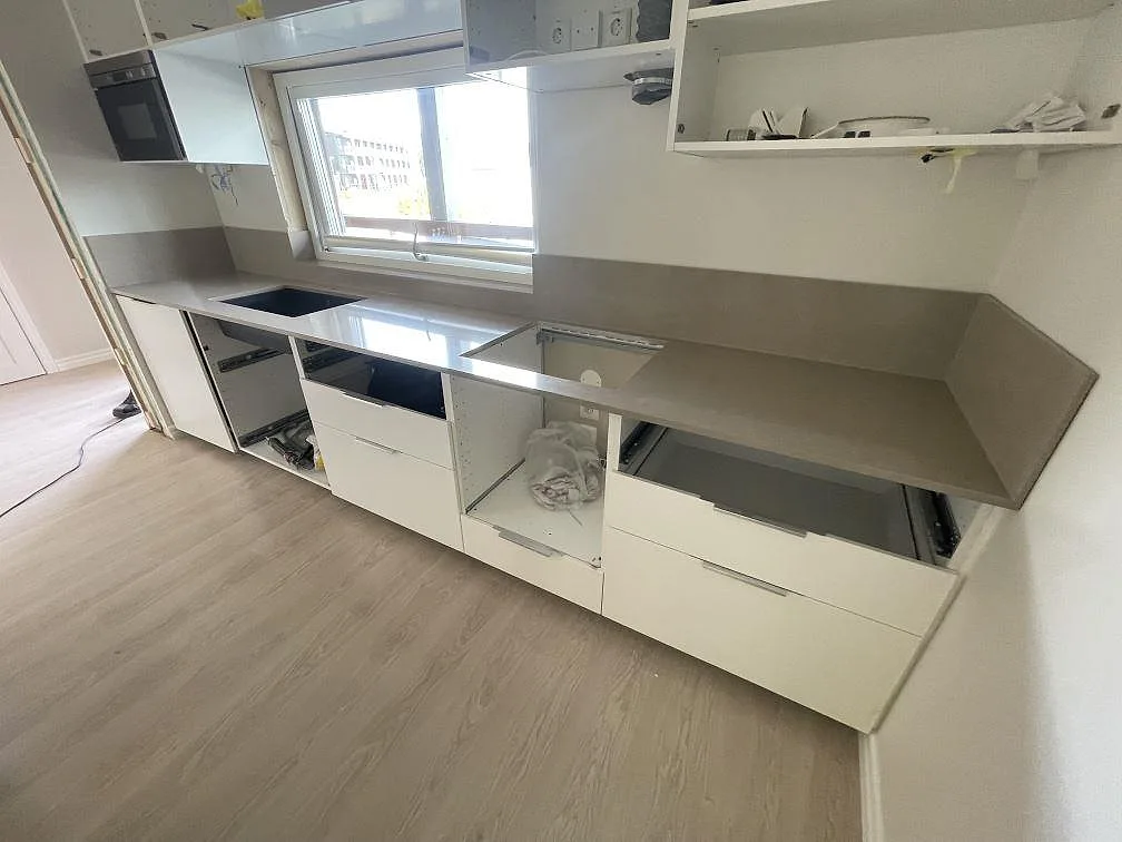 Lång köksbänkskiva i polerad Silestone Coral Clay med 12 mm uppvikt stänkskydd och öppna köksstommar under montering i Södertälje.