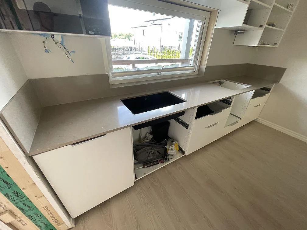 Rak bänkrad i polerad Silestone Coral Clay, gråbeige kvartskomposit, monterad under fönster med stänkskydd i ett kök i Södertälje.